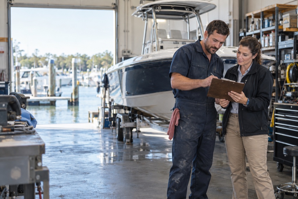 Marine dealership service advisor and technician reviewing a boat service order in a working service bay.